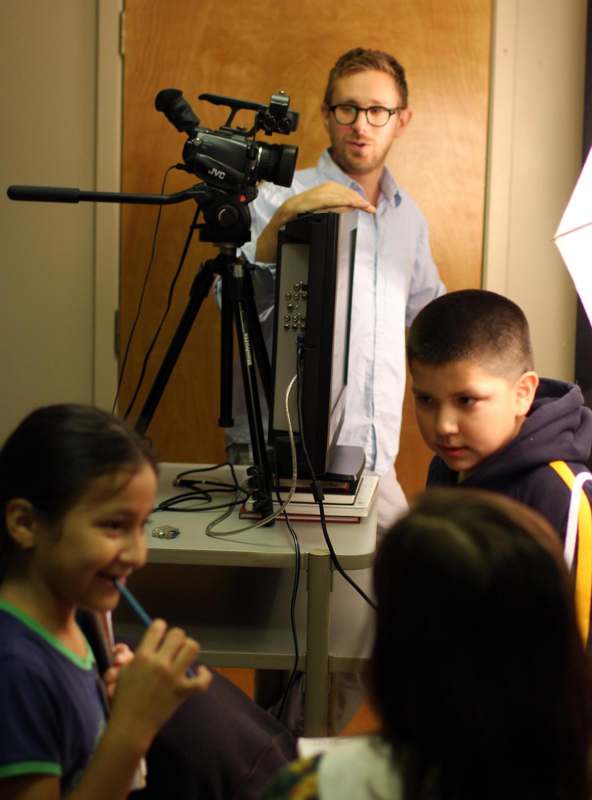 a man standing behind a camera and a group of kids