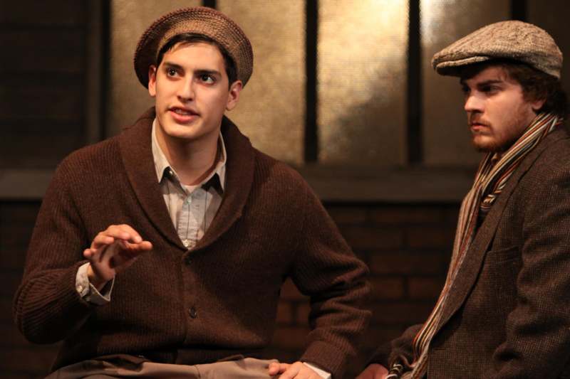 a man in a brown sweater and hat talking to another man
