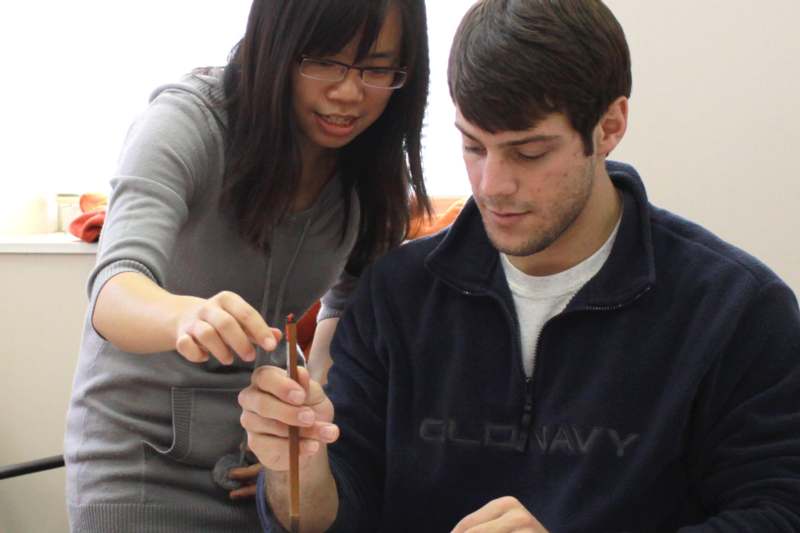 a woman standing next to a man holding a pencil