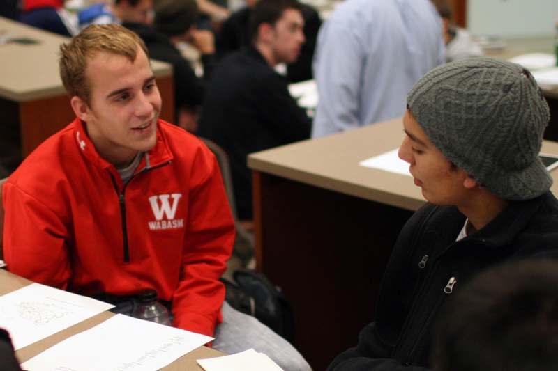 a man in a red jacket talking to a young man in a beanie