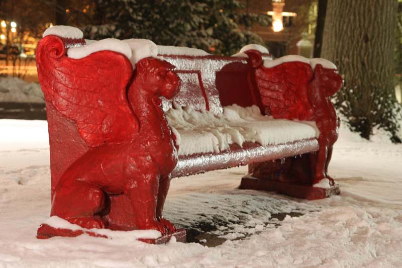 a red bench with a couple of griffins on it covered in snow