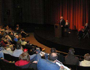 a man speaking at a podium with a crowd of people