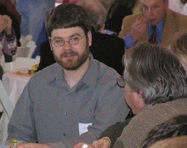 a man wearing glasses and a grey shirt talking to a man