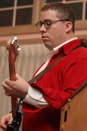 a man in red shirt and glasses playing a guitar