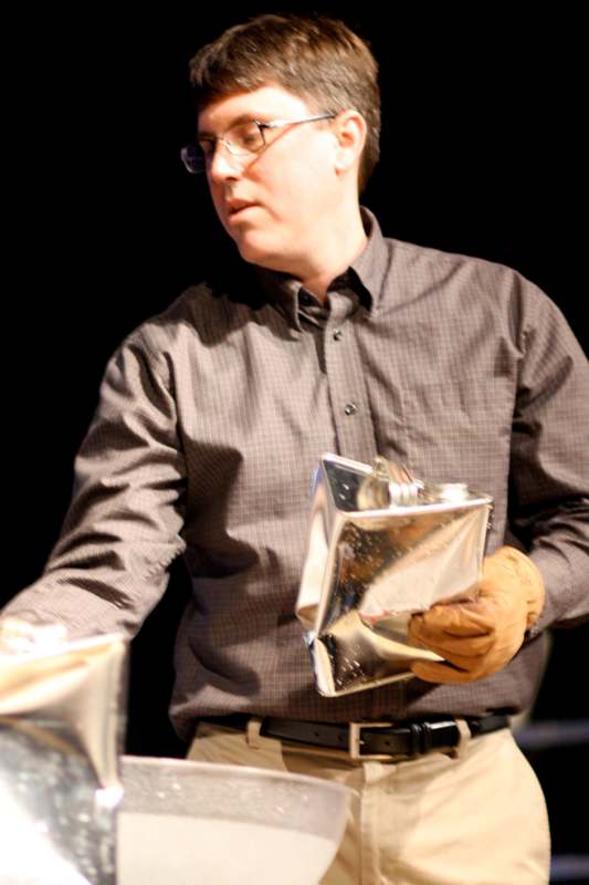 a man wearing glasses and a brown shirt holding a silver bag