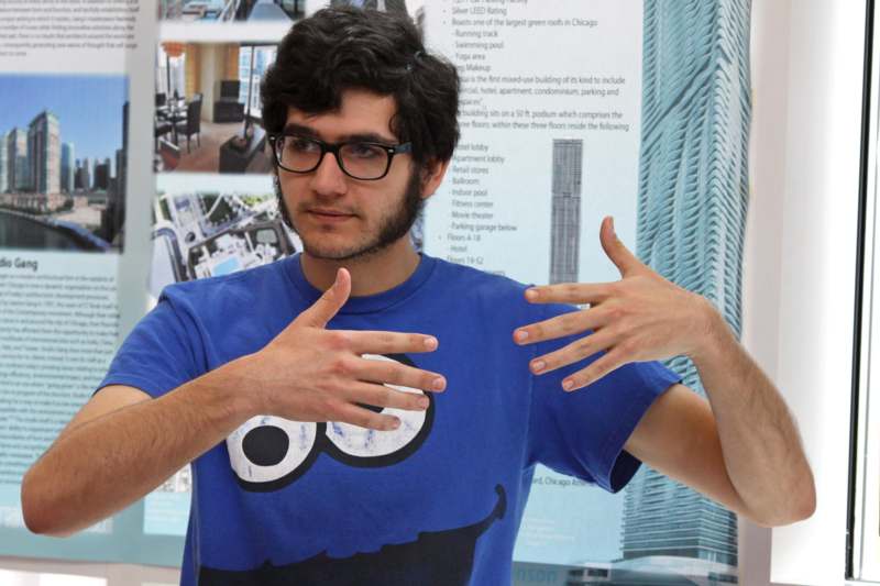 a man with glasses and a blue shirt with his hands up
