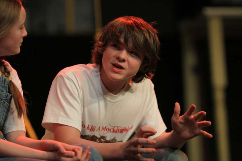 a boy sitting on a stage with his hands up