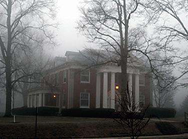 a house with columns and a tree in the fog