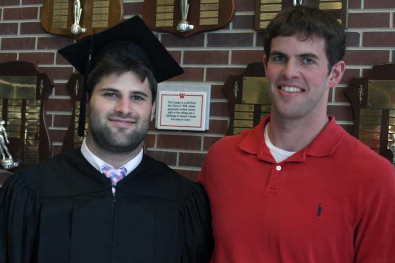 a man in a graduation gown and cap standing next to another man in a red shirt