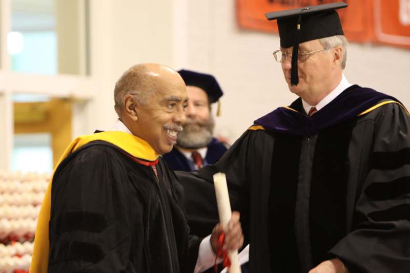 a man in a graduation gown shaking hands with another man