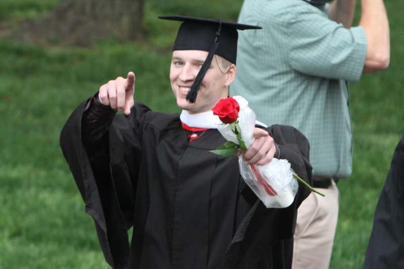 a man in a graduation gown pointing at a rose