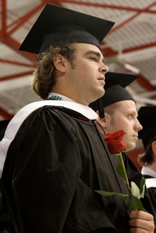 a man in graduation gown holding a rose
