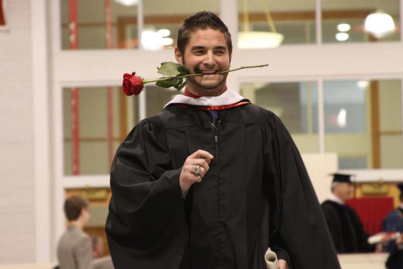 a man in a graduation gown holding a rose in his mouth