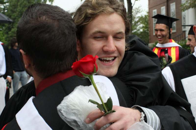 a man in a graduation gown hugging a red rose