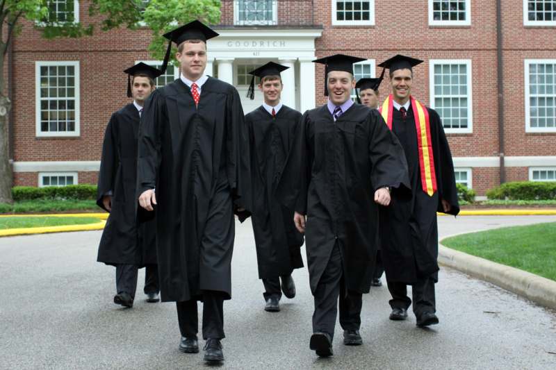 a group of men in graduation gowns and caps walking down the street