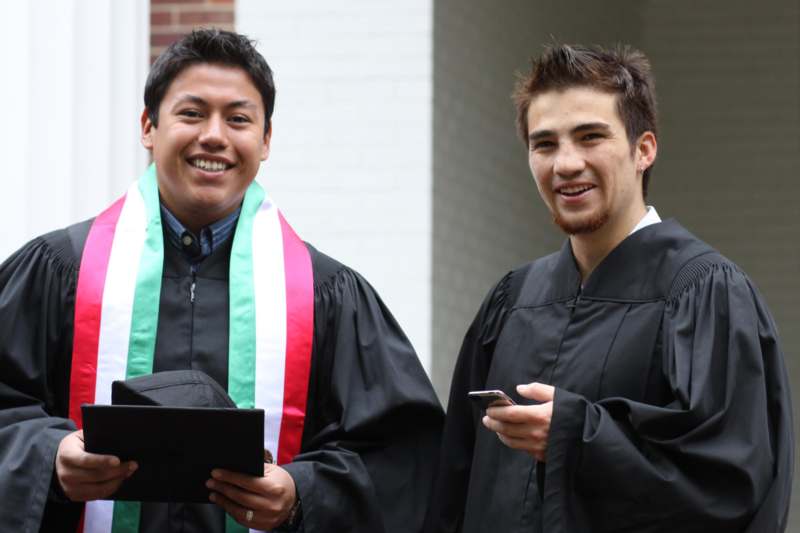 two men wearing graduation gowns and holding a tablet