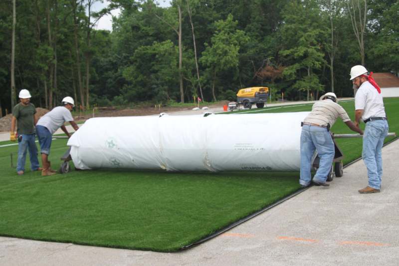 men in hardhats rolling a large white bag on a green field