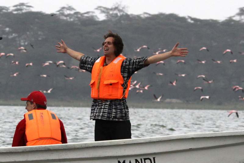 a man in an orange vest standing on a boat with arms outstretched