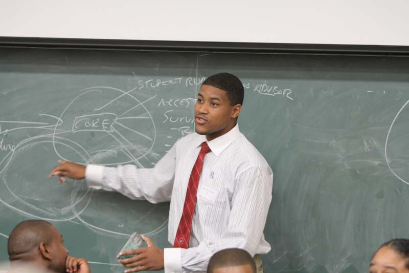 a man in a red tie pointing at a chalkboard