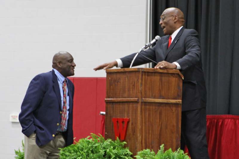 a man standing at a podium with a microphone and another man standing at the podium