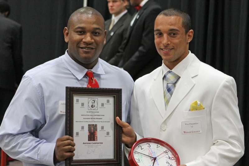 a couple of men holding a clock and a framed plaque