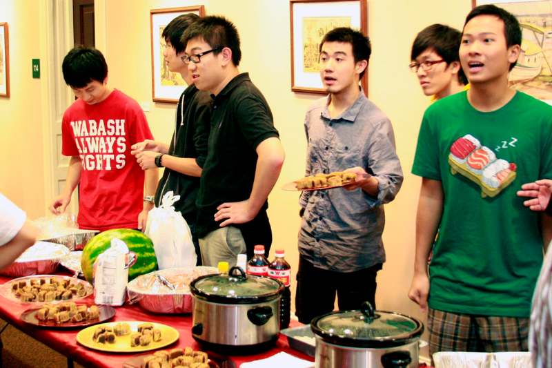 a group of young men standing around a table full of food
