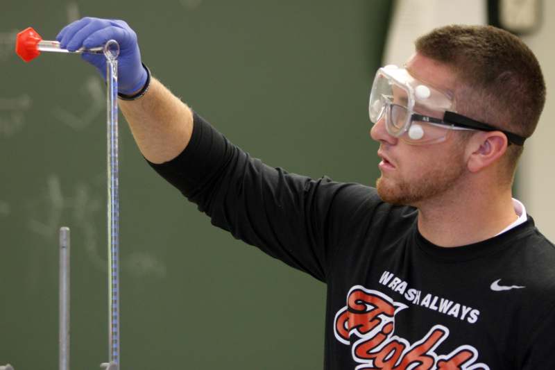 a man wearing safety goggles and gloves holding a test tube