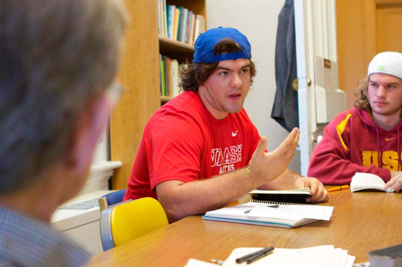 a man in a red shirt sitting at a table with a book and a man in a blue hat