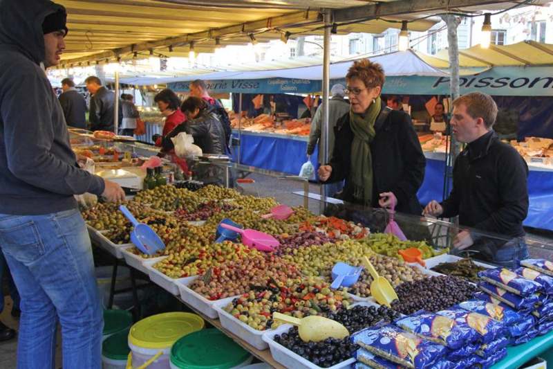 people at a market stall with many different types of olives