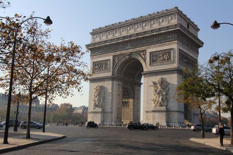 a large stone arch with statues on the sides with Arc de Triomphe in the background