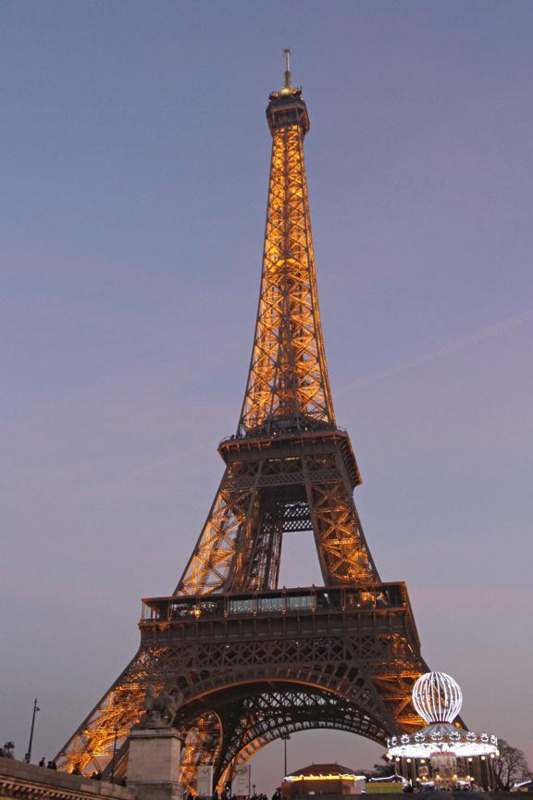 a tall metal tower with lights with Eiffel Tower in the background
