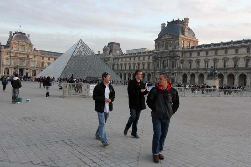 a group of men walking in front of a glass pyramid