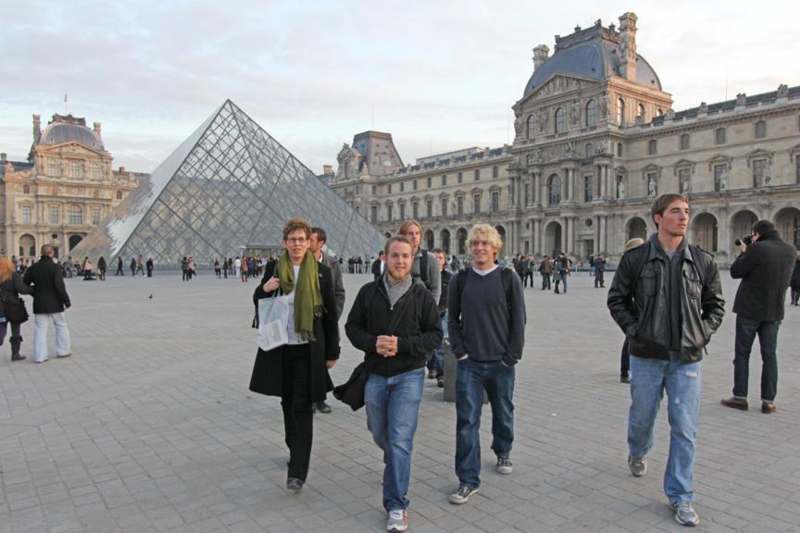 a group of people walking in front of a glass pyramid