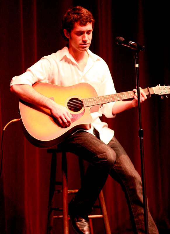 a man playing guitar on a stool