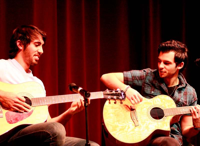 two men playing guitars on a stage