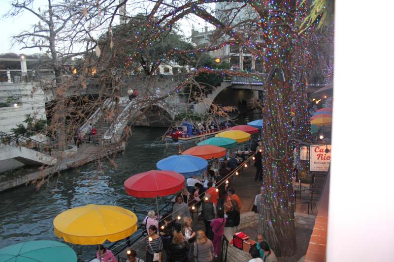 a group of people walking along a river with colorful umbrellas