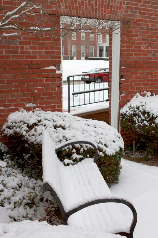 a snow covered bench outside a brick building