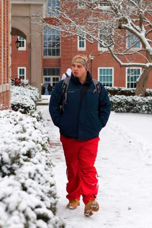 a man in red pants and a backpack walking on a snowy sidewalk