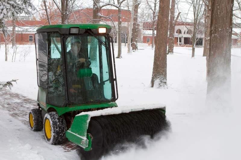 a man in a green vehicle with a green roller in the snow