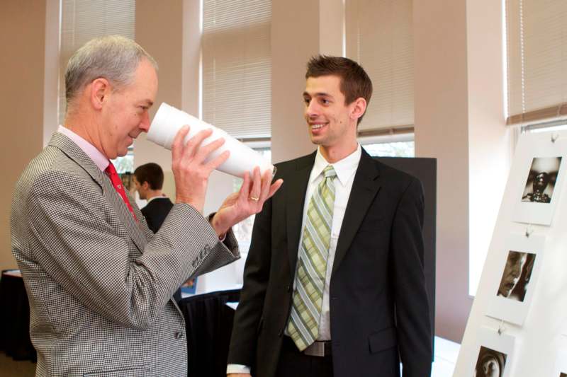 a man in suit speaking to a man in a white cup
