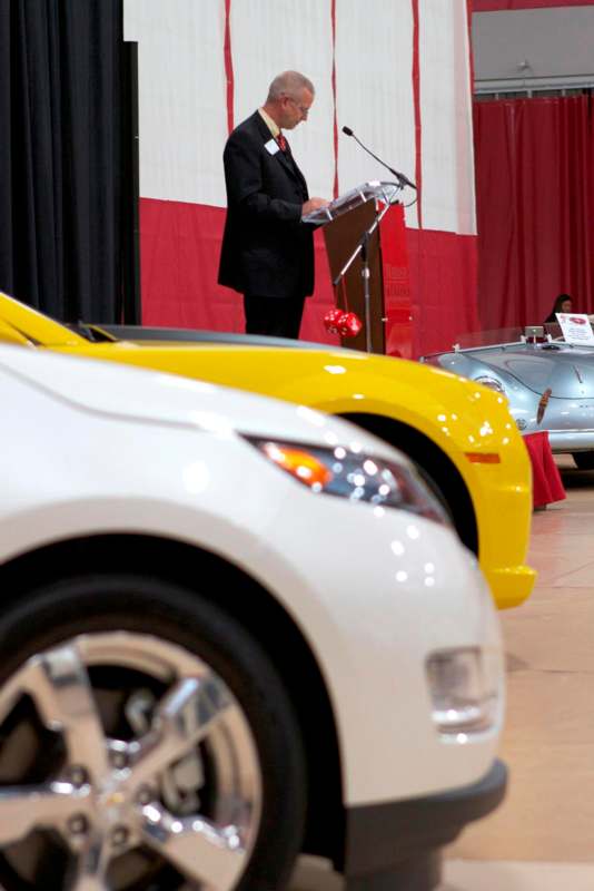 a man standing at a podium with a podium and a car behind him