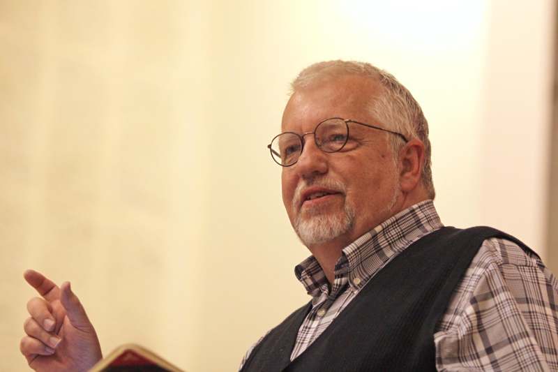 a man wearing glasses and a vest reading a book