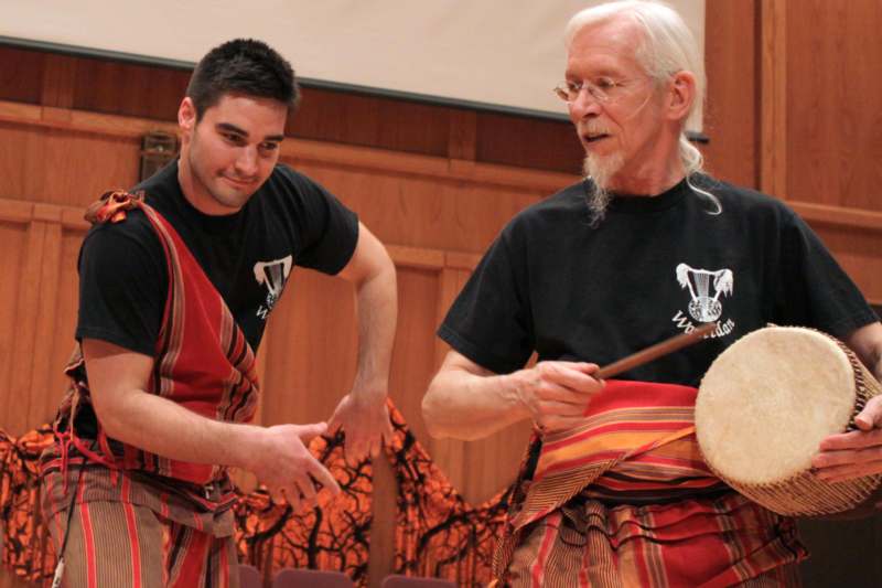 a man holding stick and another man playing drums