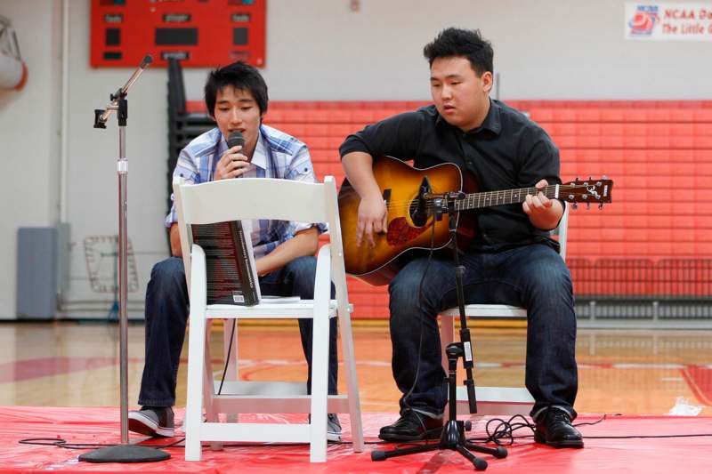a man playing guitar and singing to a man sitting in a chair