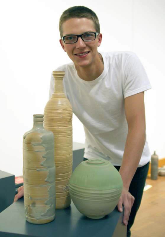 a man with glasses smiling next to several vases