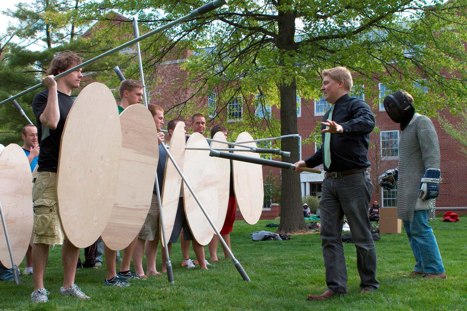 a man pointing at a group of people holding wooden shields