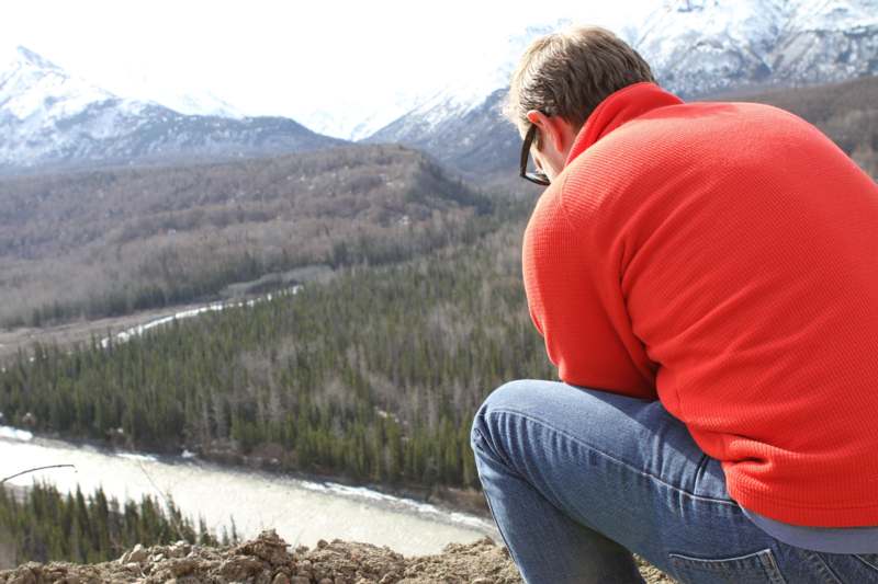 a man sitting on a cliff looking at a river and mountains