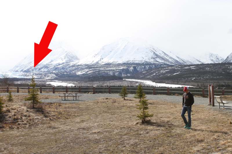a man standing in a field with a picnic table and snow covered mountains
