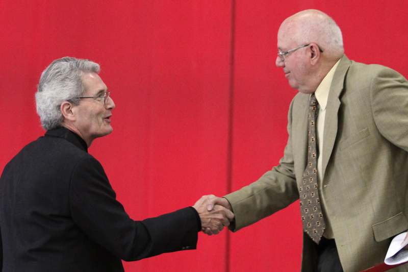 two men shaking hands in front of a red wall