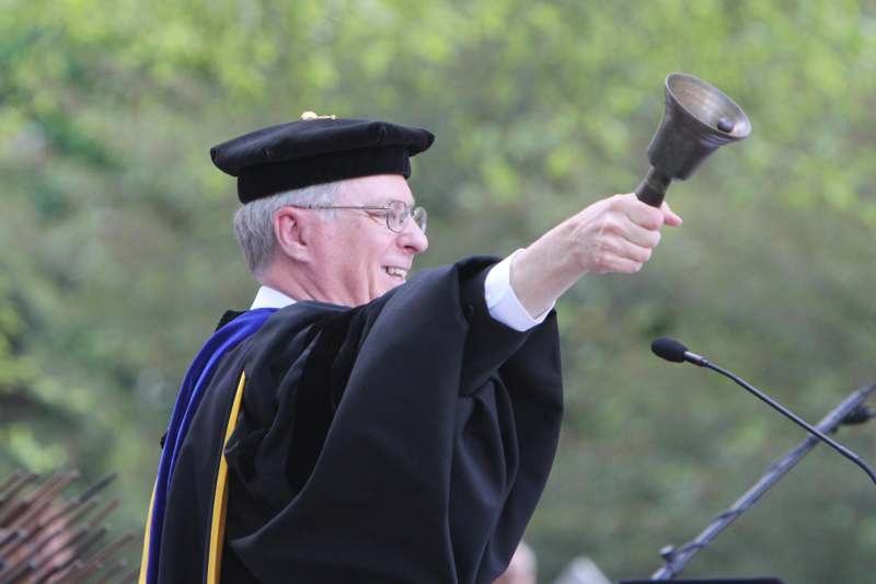 a man in a graduation gown holding a bell